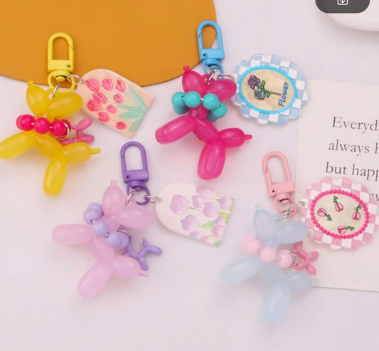 A collection of colorful balloon dog keychains with beaded collars and decorative charms, displayed on a flat surface.