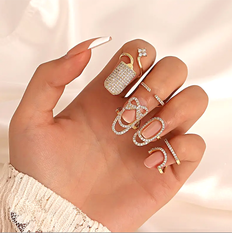 Close-up of a hand adorned with multiple gold-tone rhinestone nail rings, featuring an elegant, crystal-studded design against a soft neutral background.