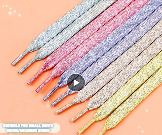 A collection of metallic glitter shoelaces in assorted colors, displayed on a peach-colored background.

