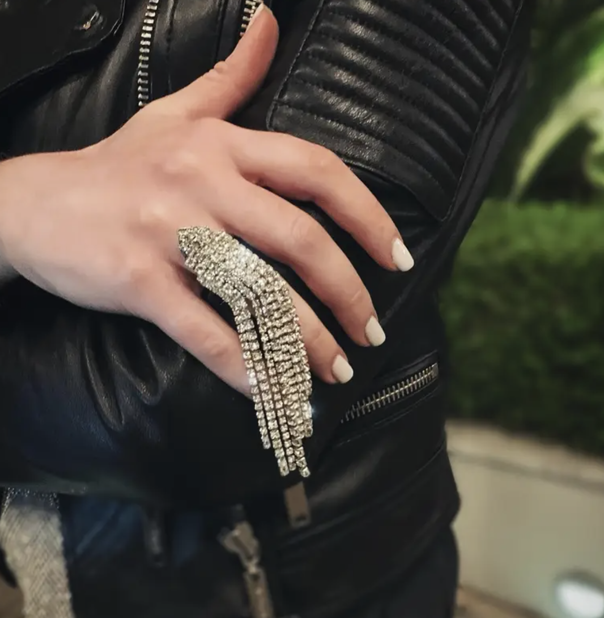 A rhinestone fringe ring with cascading crystal details, worn with a black leather jacket for an edgy yet glamorous look.